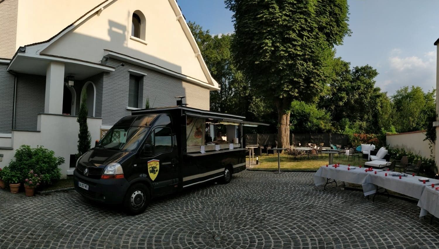 Le food truck Sergio Pizza installé dans la cour d'une maison, des tables dressées sur la pelouse.